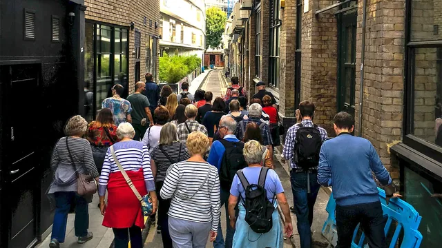 Voyage scolaire durable à Londres : groupe de visiteurs de dos suivant leur guide dans une ruelle de brique londonienne